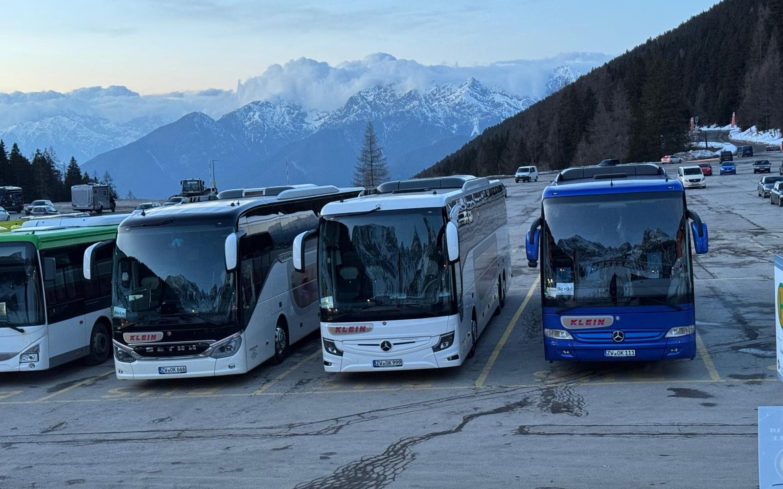 Drei Reisebusse von Omnibus Klein nebeneinander auf einem Parkplatz vor verschneiten Bergen